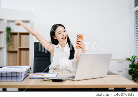 Smiling young businesswoman celebrating success at her desk with laptop, showcasing achievement, productivity, happiness, remote work and professional growth. Smiling young businesswoman celebrating success at her desk with laptop, showcasing achievement, productivity, happiness, remote work and professional growth. 140870635