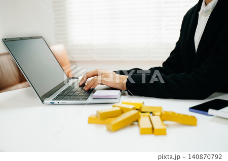 Professional working on laptop with gold bars on desk. Investment, finance, trading, wealth growth, market strategy and modern business concept. Professional working on laptop with gold bars on desk. Investment, finance, trading, wealth growth, market strategy and modern business concept. 140870792