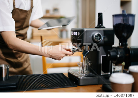Professional cafe owner preparing coffee in a modern coffee shop with espresso machine and digital tablet, showcasing small business lifestyle Professional cafe owner preparing coffee in a modern coffee shop with espresso machine and digital tablet, showcasing small business lifestyle 140871097