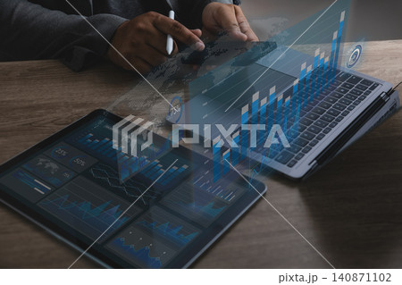 Hands using smartphone beside laptop and tablet with digital charts, analyzing financial data on a business dashboard for reporting, performance review, and management support. Hands using smartphone beside laptop and tablet with digital charts, analyzing financial data on a business dashboard for reporting, performance review, and management support. 140871102