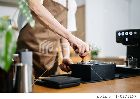 Professional barista operating coffee grinder in modern cafe kitchen, showcasing coffee preparation, small business workflow, hospitality Professional barista operating coffee grinder in modern cafe kitchen, showcasing coffee preparation, small business workflow, hospitality 140871157