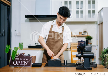 Male Asian barista using an espresso machine and taking notes on a clipboard in coffee shop. Male Asian barista using an espresso machine and taking notes on a clipboard in coffee shop. 140871164