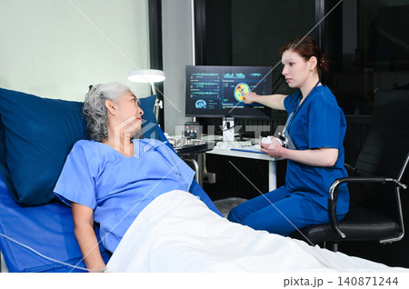 A professional nurse points to brain scan results on a monitor while consulting an elderly patient, representing medical diagnostics, neurology, 140871244
