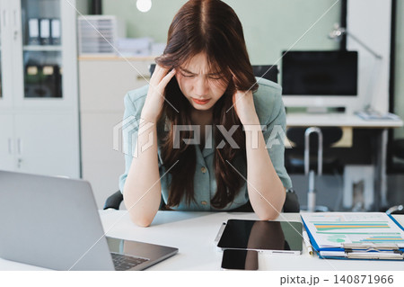 Asian businesswoman having a stressful phone call, holding a pen, and looking troubled while working on her laptop with financial documents and a calculator on her office desk Asian businesswoman having a stressful phone call, holding a pen, and looking troubled while working on her laptop with financial documents and a calculator on her office desk 140871966