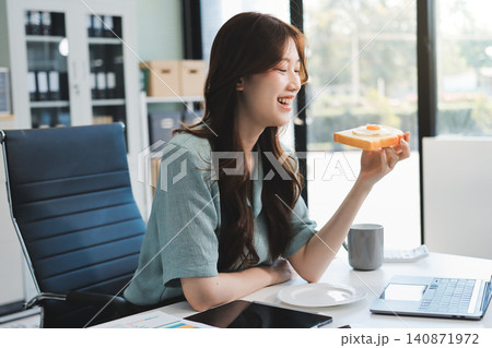 Asian woman reading book eating snack in office Asian woman reading book eating snack in office 140871972