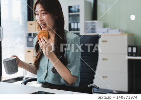 Asian woman reading book eating snack in office 140871974