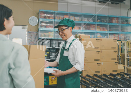 荷受けチェックをしながら笑顔で会話するスーパーのバックヤードの男性スタッフ 荷受けチェックをしながら笑顔で会話するスーパーのバックヤードの男性スタッフ 140873988