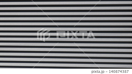 The texture of horizontal metal siding is dark gray. Smooth, parallel panels form a strict geometric pattern, where the alternating protruding edges and deep shadows create volume. The texture of horizontal metal siding is dark gray. Smooth, parallel panels form a strict geometric pattern, where the alternating protruding edges and deep shadows create volume. 140874387