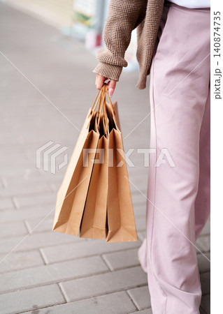 Woman holding brown paper shopping bags while standing on urban sidewalk with copy space 140874735