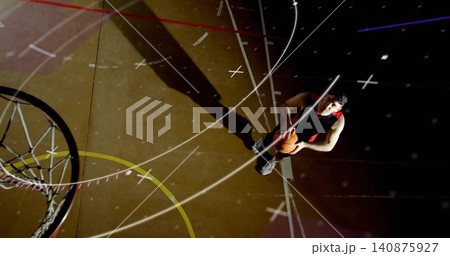 Standing basketball player in sleeveless jersey holding ball near hoop with painted lines 140875927