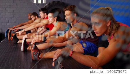 Stretching group of eight adults wearing athletic tops and shoes on rubber gym floor, with tire 140875972