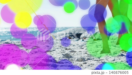 Walking woman in shorts, legs, feet on sunlit beach with rocks, horizon, colorful bokeh, copy space 140876005