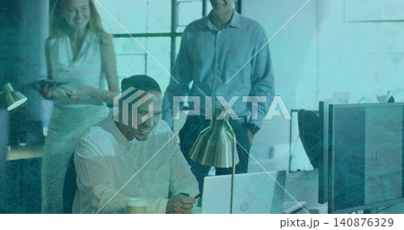 Smiling seated man wearing long-sleeve shirt holding smartphone, checking laptop at open office 140876329