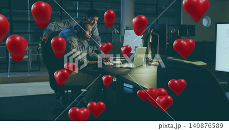 Typing seated man wearing headphones, buttoned shirt at office desk, with laptop and heart balloons Typing seated man wearing headphones, buttoned shirt at office desk, with laptop and heart balloons 140876589