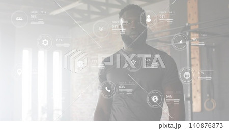 Standing fit man wearing dark fitted athletic shirt in warehouse gym, HUD, pull-up rig, rings 140876873