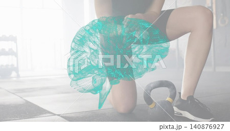 Kneeling woman wearing shorts and sneakers presenting teal 3D brain mesh on gym floor, kettlebell 140876927