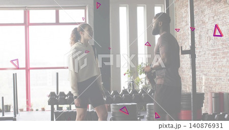 Talking trainer and client wearing athletic apparel standing in loft gym, with dumbbells and plates Talking trainer and client wearing athletic apparel standing in loft gym, with dumbbells and plates 140876931