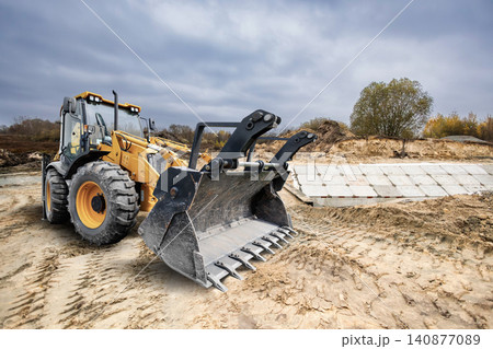Universal excavator loader performs tasks at a construction site by moving soil and clearing land for upcoming development projects in outdoor space 140877089