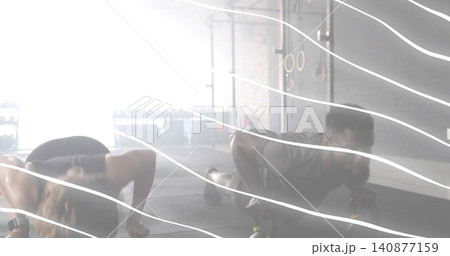 Two adults performing partnered push-ups on handles at gym, wearing sports top, leggings, shorts Two adults performing partnered push-ups on handles at gym, wearing sports top, leggings, shorts 140877159