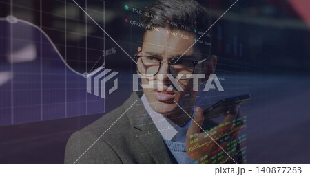 Holding smartphone, executive in grey blazer with glasses speaking at office, with financial charts 140877283