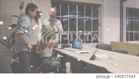High-fiving seated woman wearing knit beanie and white tank top in conference room, with laptop 140877343