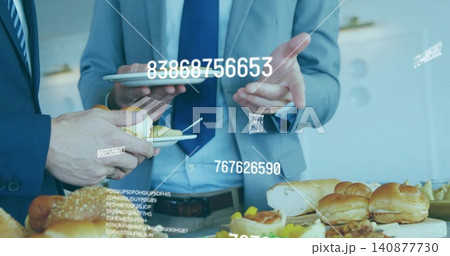 Gesturing with tablet, two men in suits holding plates at office buffet with data overlays Gesturing with tablet, two men in suits holding plates at office buffet with data overlays 140877730