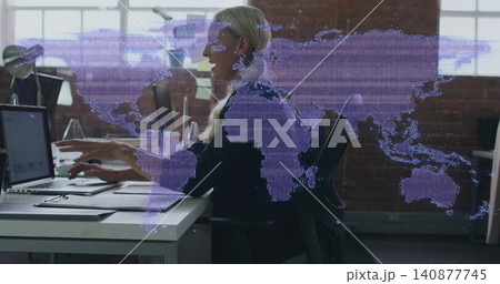 Typing blonde woman in dark blazer working on laptop at open office, with purple world-map overlay Typing blonde woman in dark blazer working on laptop at open office, with purple world-map overlay 140877745