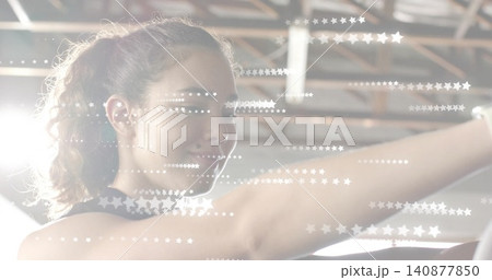 Stretching woman reaching forward at gym, wearing dark tank, with beams, ceiling light, star flares 140877850