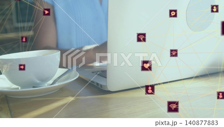 Typing woman in light blue top at cafe wooden table with silver laptop, cup, network icons 140877883