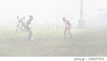 Handling ball, left player dribbling as right defender crouching on foggy pitch with cones, pinnies 140877933