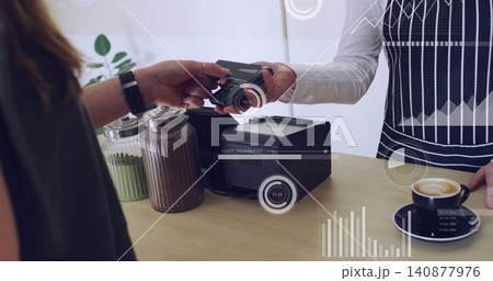 Handing card, customer passing to barista in striped apron holding reader at cafe, jars latte HUD 140877976