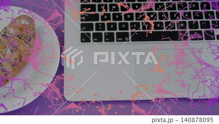 Showing silver laptop, black keys and pad on purple mat, croissant on plate, pink-orange confetti Showing silver laptop, black keys and pad on purple mat, croissant on plate, pink-orange confetti 140878095