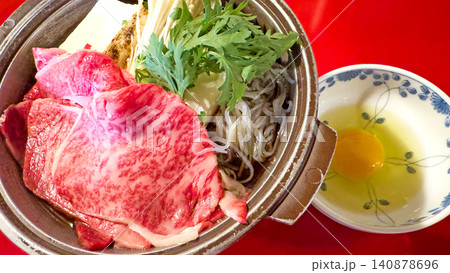 赤いテーブルの上に置かれた霜降り牛肉と生卵付きのすき焼き鍋 赤いテーブルの上に置かれた霜降り牛肉と生卵付きのすき焼き鍋 140878696