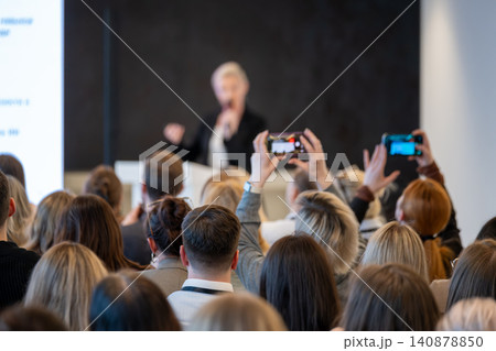 Audience recording speaker at conference presentation, attendees using smartphones to capture professional talk 140878850