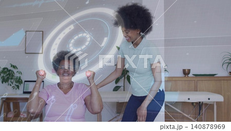 Older woman in pink shirt performing arm curls in therapy, therapist supporting pink weights and AR Older woman in pink shirt performing arm curls in therapy, therapist supporting pink weights and AR 140878969