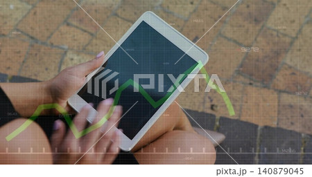 Holding white tablet, adult female tapping screen on outdoor step, wearing dark shorts, green graph Holding white tablet, adult female tapping screen on outdoor step, wearing dark shorts, green graph 140879045