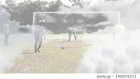 Defending soccer players in sportswear forming line on park pitch with metal goal, ball and fog Defending soccer players in sportswear forming line on park pitch with metal goal, ball and fog 140879151