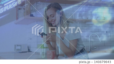 Smiling woman wearing gray tee, denim, scrolling phone in kitchen, pink mug, sink, digital overlay Smiling woman wearing gray tee, denim, scrolling phone in kitchen, pink mug, sink, digital overlay 140879643