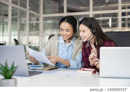 Operators in headsets pointing at document near laptop 140880587