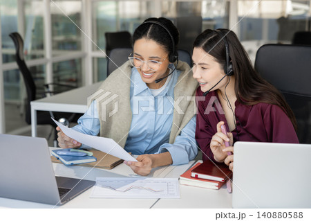 Smiling coworkers in headsets reviewing business papers 140880588