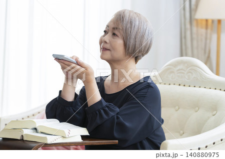 ソファーに座りスマホで英会話の学習をするシニア女性 140880975