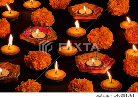 Diwali festival concept with lit clay diyas and marigold flowers on black background Diwali festival concept with lit clay diyas and marigold flowers on black background 140881361