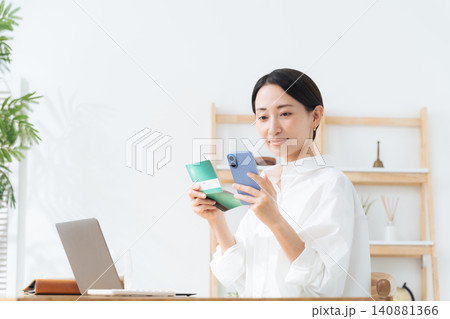 スマホと通帳を見る女性。貯金、金融、アプリ、銀行、マネー、お金、家計、キャッシュレス決済、電子マネー スマホと通帳を見る女性。貯金、金融、アプリ、銀行、マネー、お金、家計、キャッシュレス決済、電子マネー 140881366