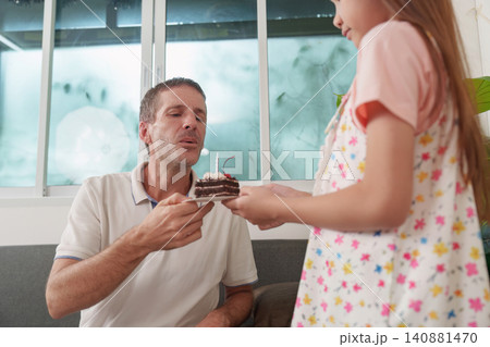Young daughter presenting birthday cake to her father at home for celebration 140881470