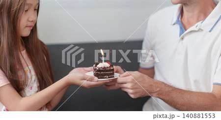 Cropped hands of father and daughter holding birthday cake with lit candle 140881553