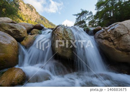 Water cascades over large stones in a serene mountain stream during midday Water cascades over large stones in a serene mountain stream during midday 140881675