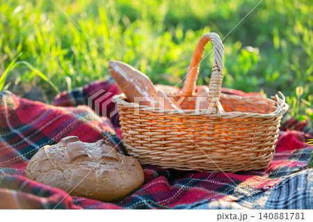 Picnic basket with freshly baked bread placed on a checkered blanket in a sunny meadow setting Picnic basket with freshly baked bread placed on a checkered blanket in a sunny meadow setting 140881781