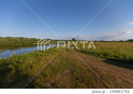 Picturesque riverside path inviting nature lovers for a serene walk in the afternoon sunshine with vibrant greenery surrounding Picturesque riverside path inviting nature lovers for a serene walk in the afternoon sunshine with vibrant greenery surrounding 140881782