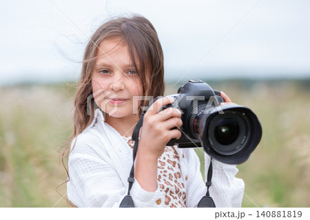 Young girl enjoys outdoor photography while holding a camera in a grassy field on a cloudy day Young girl enjoys outdoor photography while holding a camera in a grassy field on a cloudy day 140881819