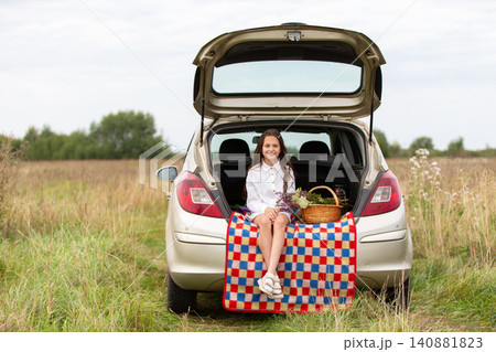 Girl enjoys a picnic by her car in a grassy field on a calm day 140881823